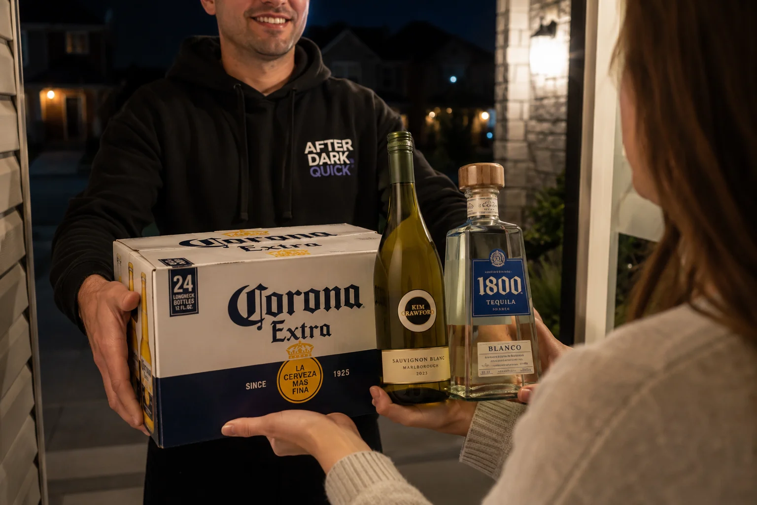 An After Dark Quick driver in a branded hoodie handing over a 24-case of Corona Extra, a bottle of Kim Crawford Sauvignon Blanc, and a bottle of 1800 Blanco tequila to a customer at her front door after dark — the beer, wine and spirits a corner-store cooler cannot carry