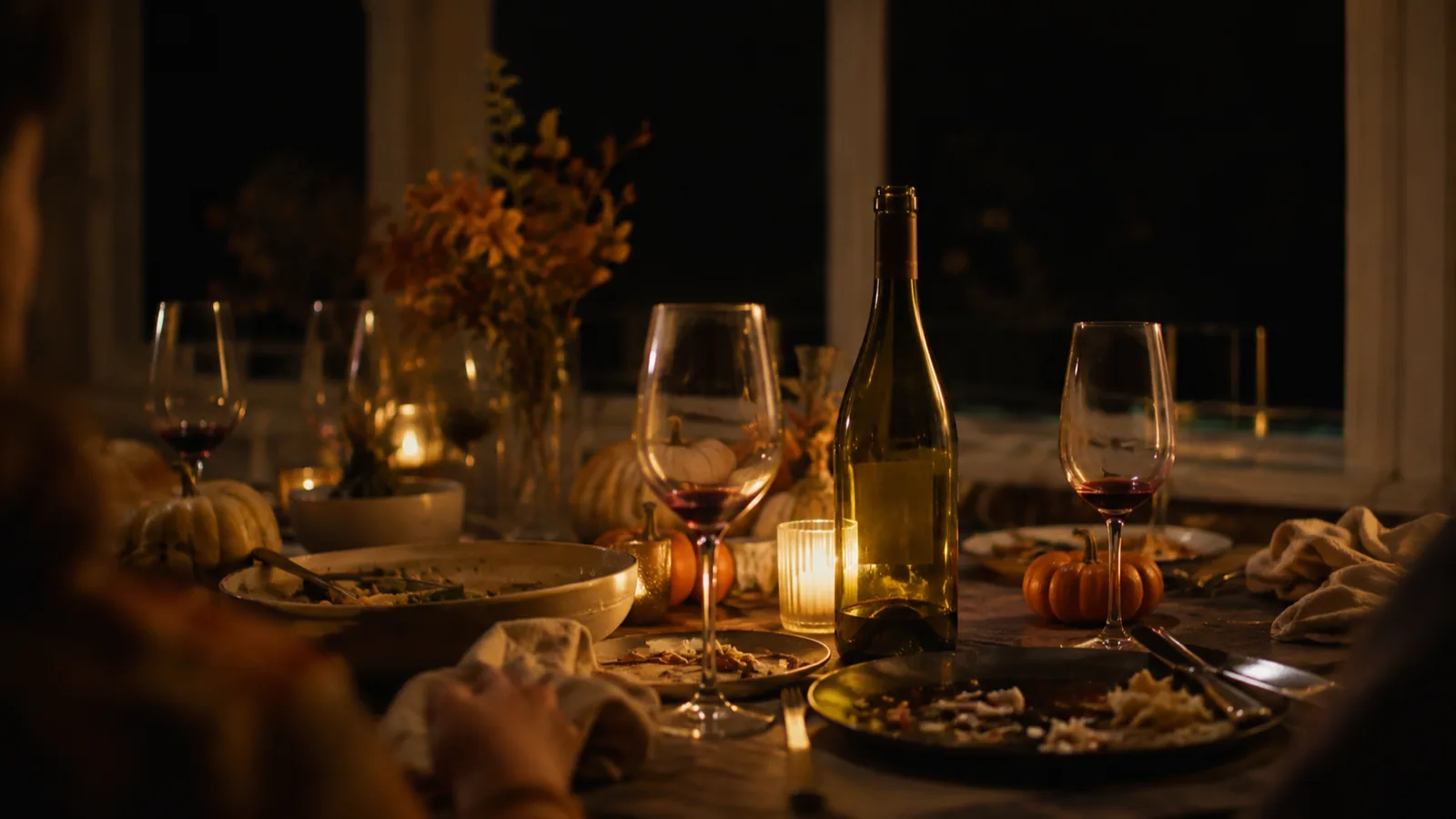 A Thanksgiving dinner table late in the evening, glasses poured and one nearly empty wine bottle standing among the plates, hours after the last store closed